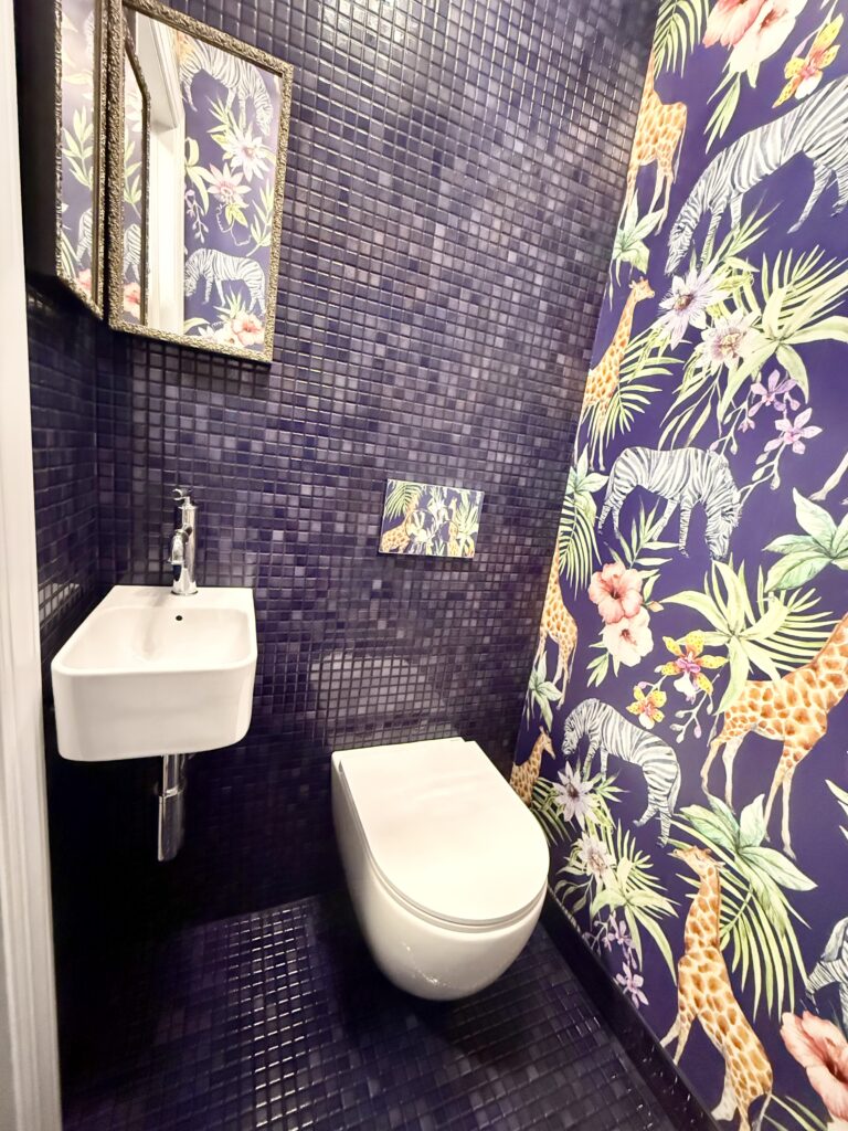 photo of the finished row house powder room showing purple floor & wall tile, purple wallpaper with safari animals, a small white sink, and a white toilet