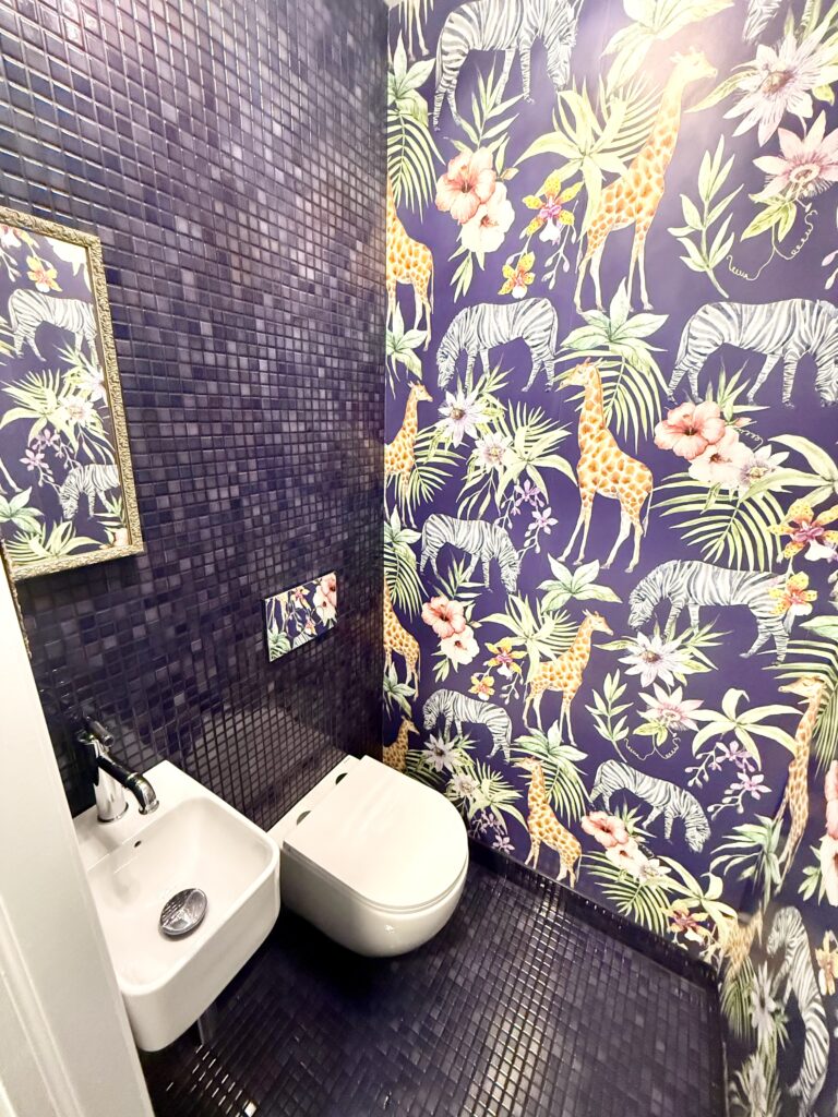 photo of the finished row house powder room showing purple floor & wall tile, purple wallpaper with safari animals, a small white sink, and a white toilet
