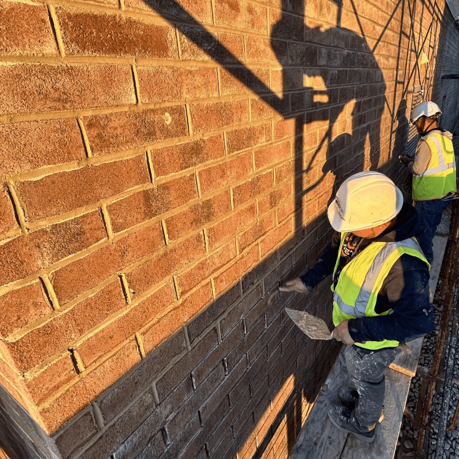Worker grinding out old mortar joints from brick wall before repointing process