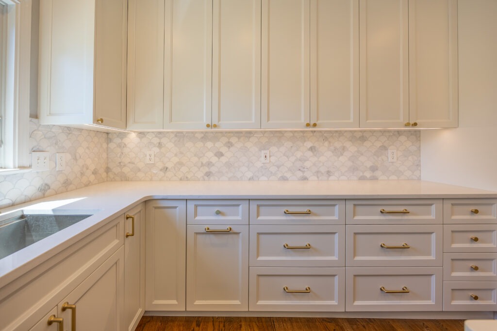 White kitchen cabinets with brass hardware, marble scallop backsplash.