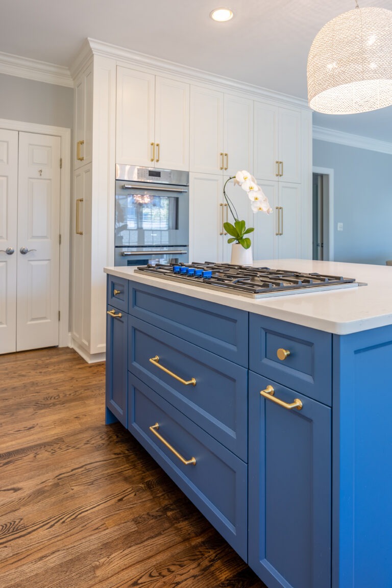 Blue kitchen island with paneled drawers, brass hardware, white perimeter cabinets, and quartz countertop.
