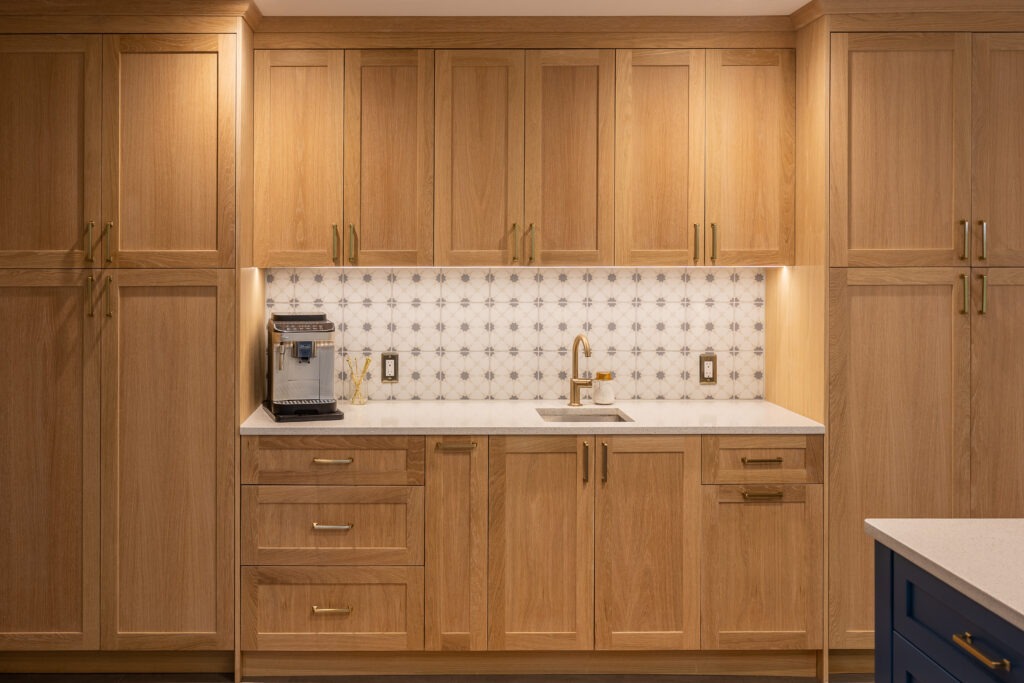 Wood built-in kitchen cabinetry with tall pantry cabinets, coffee bar, under-cabinet lighting, and brass hardware.